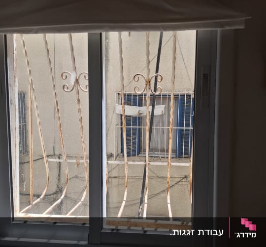 חלון עם סורגים חלודים מול בניין